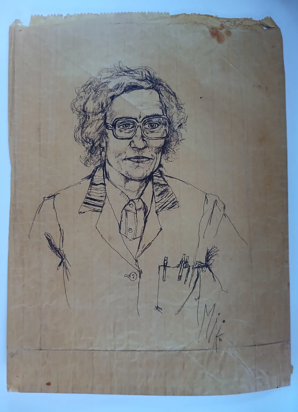 A biro portrait on a creased brown paper bag of a person with curly hair and large glasses, wearing a work coat with pens in the breast pocket, signed Mik