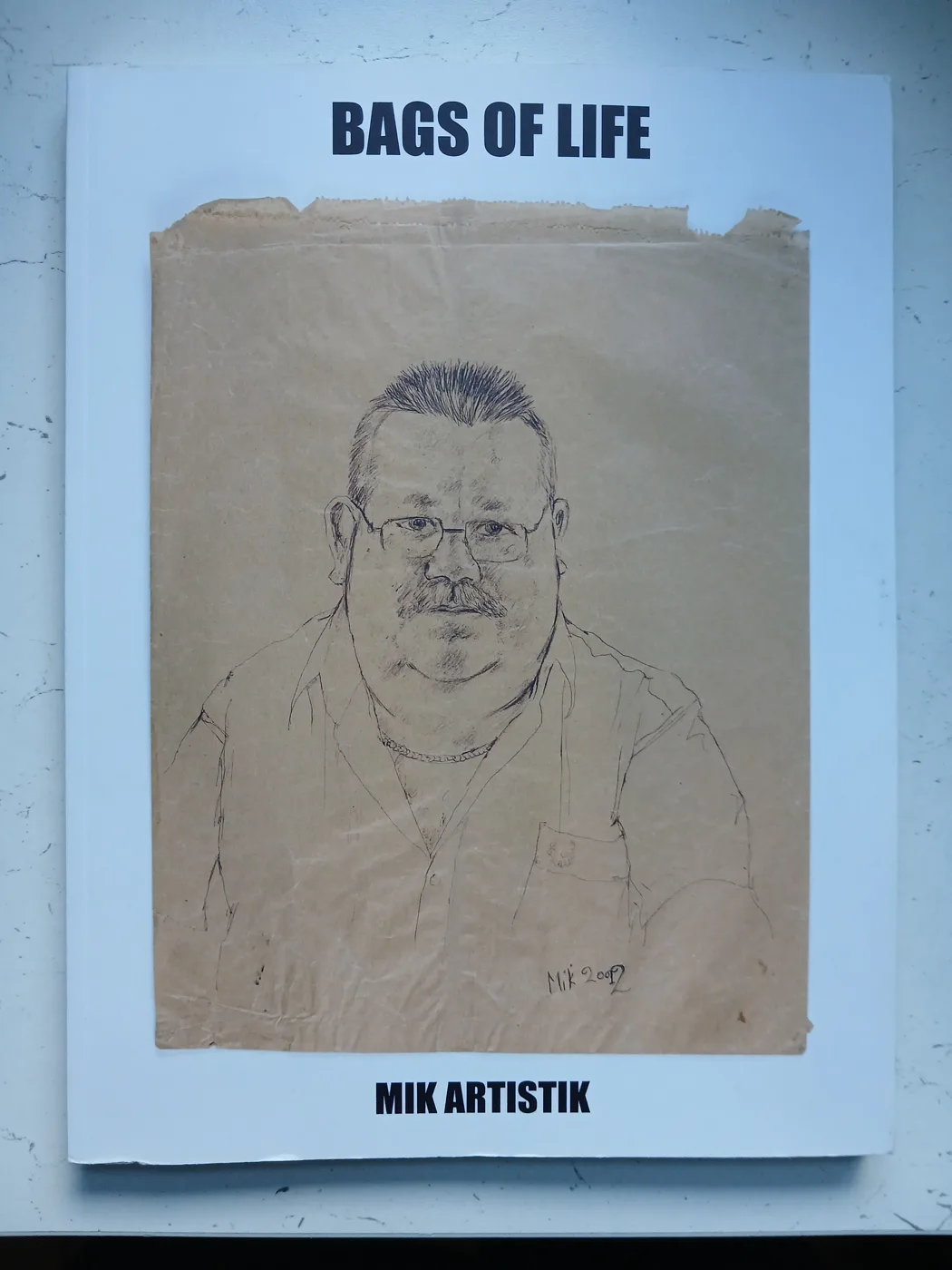 The cover of the book Bags of Life by Mik Artistik, showing a biro portrait on a brown paper bag of a man with glasses and a moustache