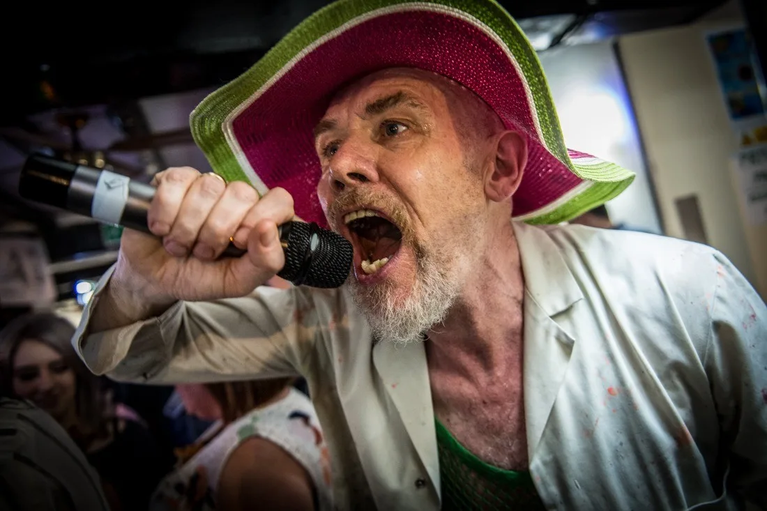 Mik Artistik singing into a microphone in a green and pink hat
