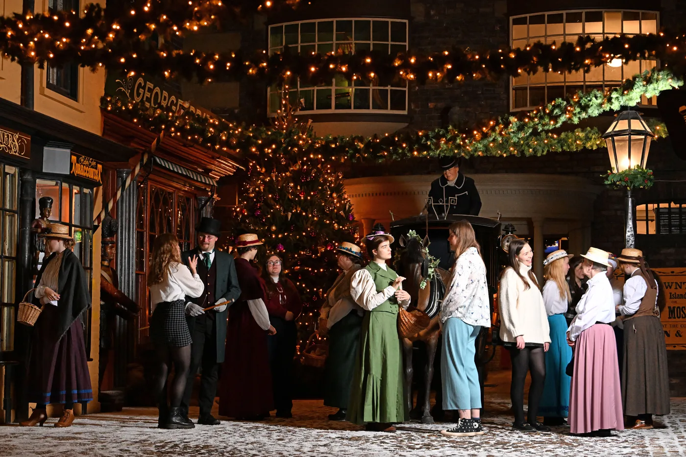 Performers in Victorian costume and visitors gathered on Kirkgate beside a horse-drawn carriage and a lit Christmas tree
