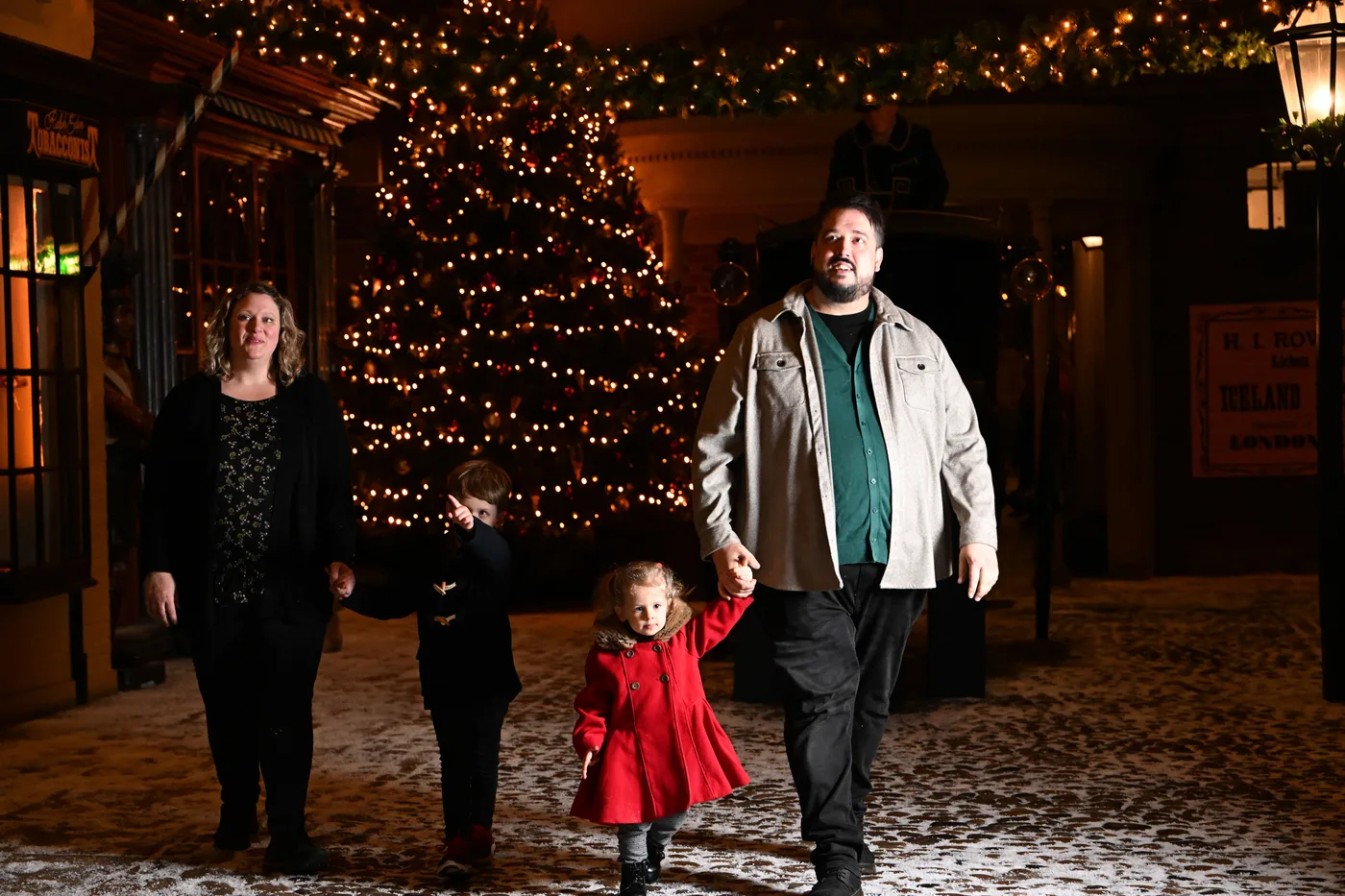 A family of four walking hand in hand along snowy Kirkgate in front of the Christmas tree