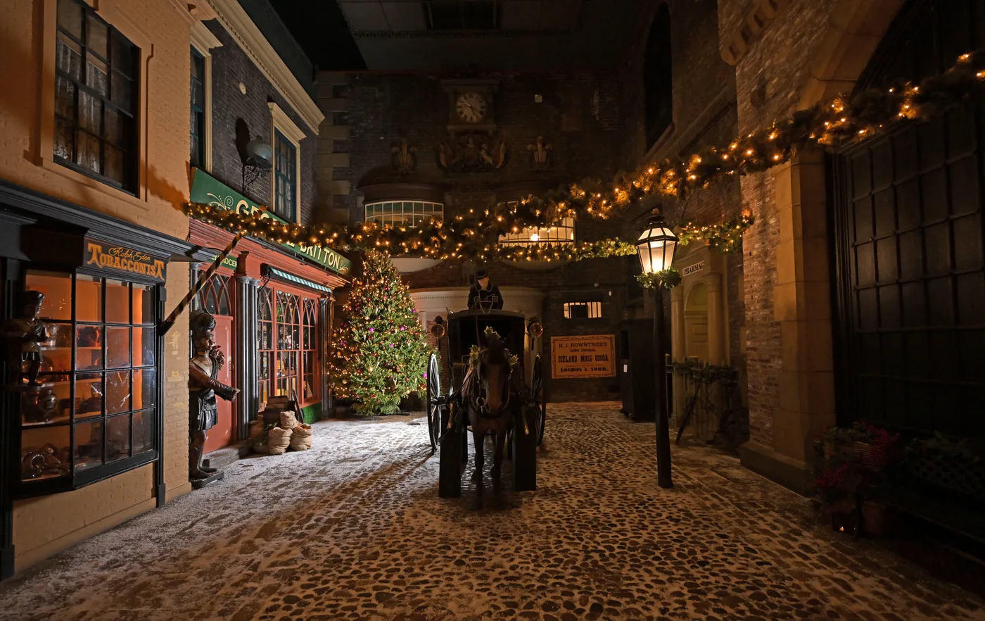 The cobbled Victorian street of Kirkgate with garlands, a lit tree, a lamp post and a horse and carriage
