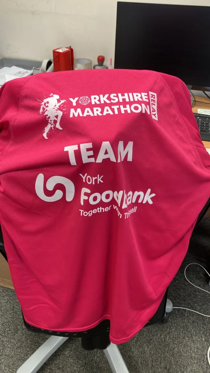 A pink Yorkshire Marathon team running shirt printed with Team York Foodbank, hung over the back of an office chair