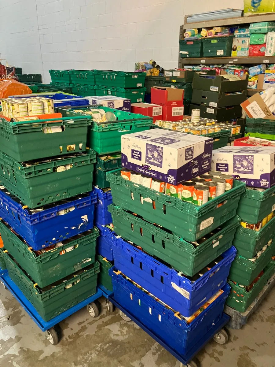 Green and blue crates of tinned and packet food stacked several high on trolleys in a warehouse