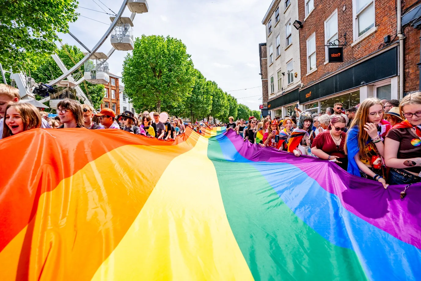 Crowds carrying a giant rainbow flag along the York Pride parade