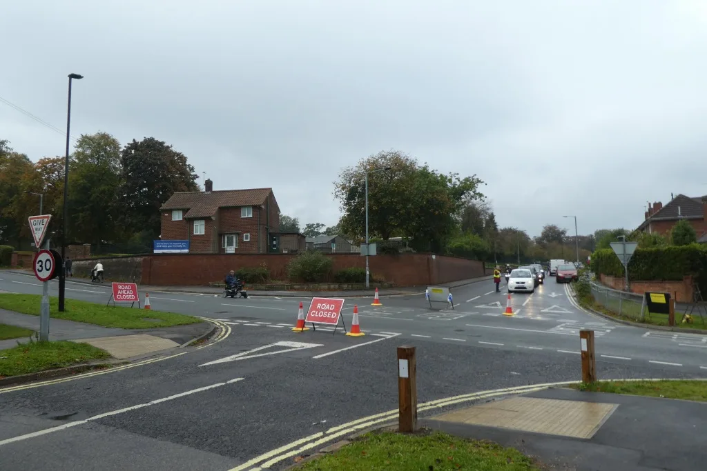 Road closed signs and a marshal at the crossroads of Thief Lane and Green Dykes Lane in York during the Yorkshire Marathon, with queuing cars beyond